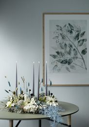 Advent wreath of poinsettias, florals and blue candles on round table in front of art print