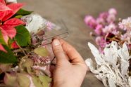 Hand heftet mit Efeunadeln getrocknete Floralien an den oberen Rand des Strohrömers.