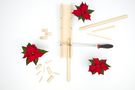 Ein Rundholz liegt mit angesetzter Säge in der Gehrungsschneidlade neben Weihnachtssternen und  Holzstücken.