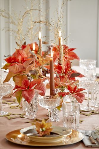 Festligt dækket bord med rustiklys, julekugler, dekorative stjerner, krystalvaser med afskårne julestjerner og græsstrå i