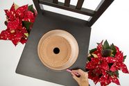 Next to two poinsettias is a black chair with a terracotta pot. One hand draws a circle around the pot with chalk.