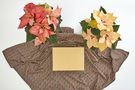 A pink and a cream-coloured poinsettia stand next to a piece of fabric spread out with an object on it.