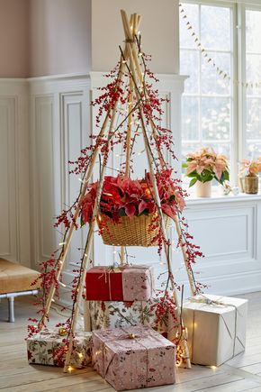 Gifts under a modern homemade wooden Christmas tree decorated with poinsettias, ilex verticillata (winterberry) and fairy lights in a bright old apartment.