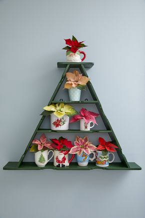 Triangular green wooden wall shelf with retro Christmas mugs filled with colourful mini poinsettias