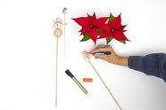 Hand drawing with pen on homemade snowman flower sticks next to red poinsettias.