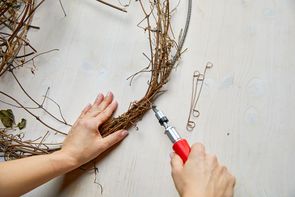 Hands attach vines to a ring with drill and twist wires.