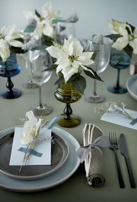 Table dressée avec assiettes, couverts, verres, serviettes et poinsettias blancs dans des verres.