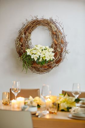 Corona de vid con poinsettia blanca en la pared junto a una mesa festiva