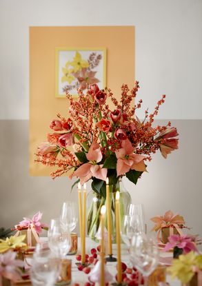 Orange arrangement of poinsettias, amaryllis and ilex verticillata (winterberry) on a colourful festive table with yellow candles