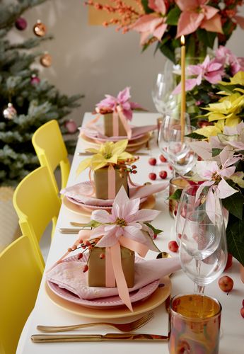 Mesa festiva en tonos pastel con sillas amarillas, regalos y centro de flores de Pascua.