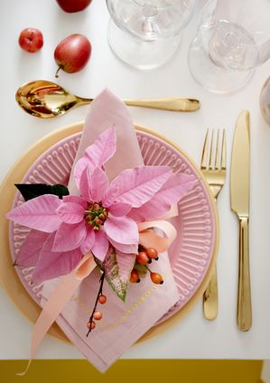 Service de table dans des couleurs pastel avec des couverts dorés et un poinsettia rose sur l'assiette.