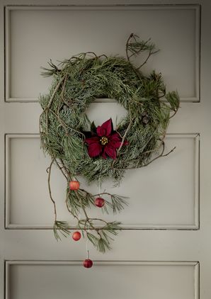 Thuja-Kranz mit Weihnachtsstern, Kiefernzweigen und Zieräpfeln an Holztür