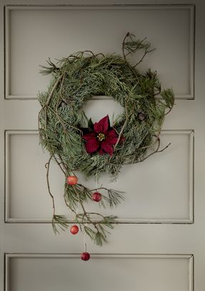 Cypress wreath with poinsettia, pine branches and crab apples on wooden door