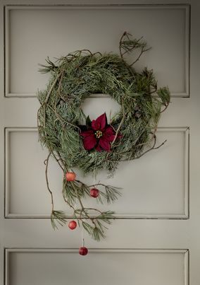 Ghirlanda di rami di pino con poinsettia e mele selvatiche appesa su una porta di legno