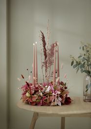 Advent wreath with ornamental grasses and cut poinsettias in pink, rose and apricot on round wooden table.