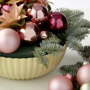 Schale mit Steckschaum und Tannengrün, Christbaumkugeln und geschnittenen Weihnachtssternen