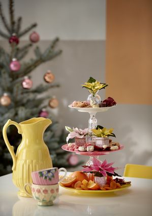 DIY upcycled cake stand made of tableware with poinsettias in tins and vintage jug and cups (on table)